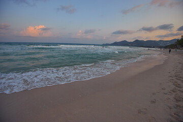 Tranquil shoreline bathed in the soft hues of sunset, with gentle waves rolling onto the beach
