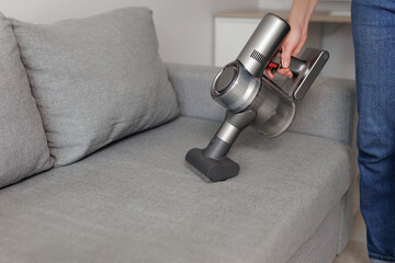 close up of woman cleaning sofa with vacuum cleaner
