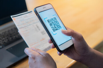 Male hands using a mobile phone to scan the QR code for the bill through the app. Convenient,...