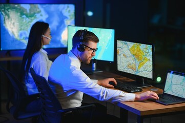 Center of dispatching maintenance. Portrait of cheerful woman and man working via headset microphone while sitting on navigation controller board