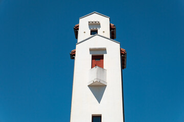 Torre de um farol em forma quadrada com algumas janelas de cor ao estilo basco num fundo com céu...