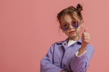 Showing thumb up. Cute little girl is against pink background