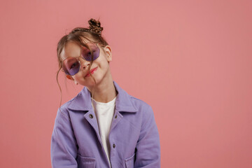 In stylish sunglasses. Cute little girl is against pink background