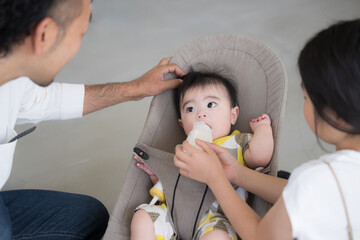 Father and sister taking care of baby Sister feeding baby and father looking on