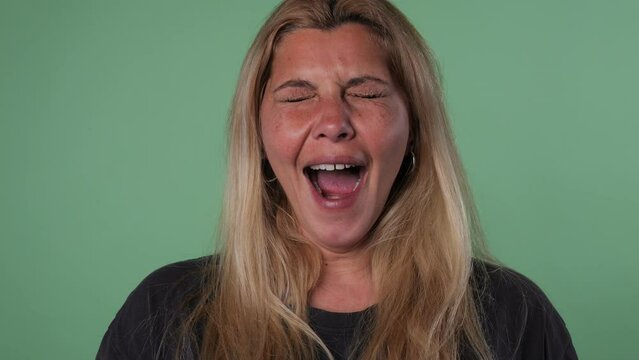 Face of a blonde adult woman yawning in green background