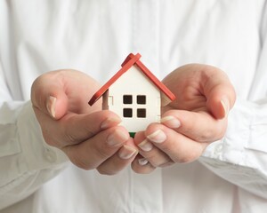 A woman dressed in a white shirt holds a small house in front of her