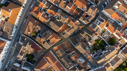 Aerial view of the charming historic streets of Évora, Portugal. Cobblestone roads wind past ancient buildings under the golden sunlight.