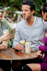 Handsome man with female friends having a drink together - Diverse young people sitting at bar...