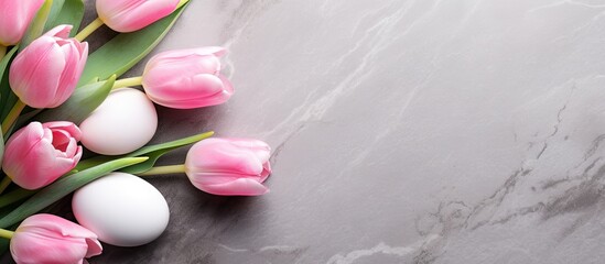 A copy space image featuring pink tulips and Easter eggs arranged on a stone surface