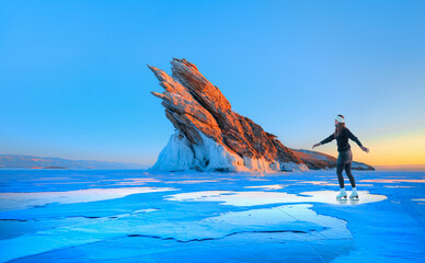A young happy woman is skating on the transparent ice of the frozen Lake Baikal on a sunny winter...