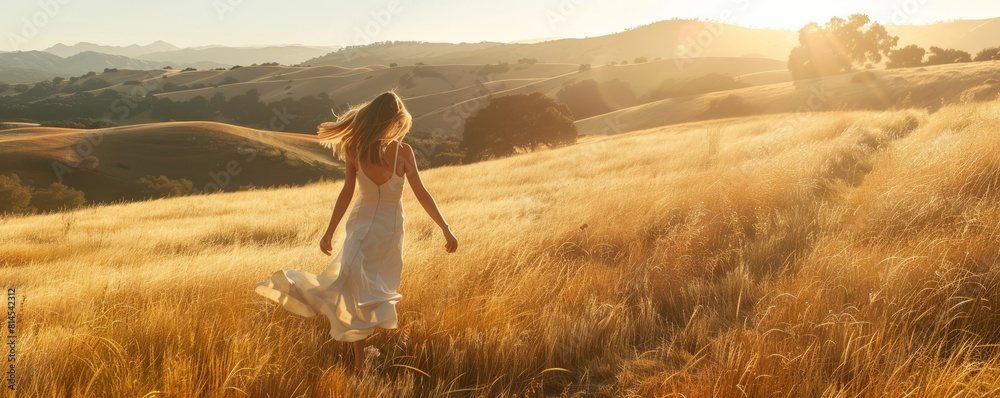 Wall mural Woman balancing in a field of golden grass in sun drenched hills of California.