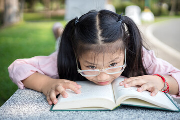 Cute little asian girl reading a book while lying at garden