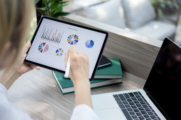 Business woman sitting at table and taking notes in tablet screen graphics and charts