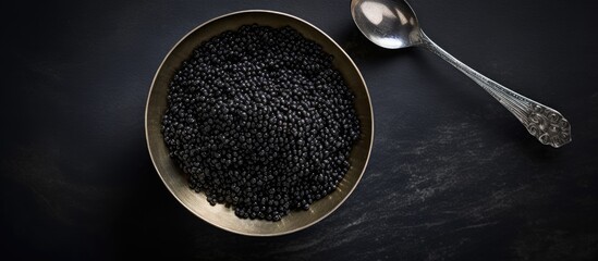 Copy space image of a bowl filled with delicious black caviar and an elegant vintage silver spoon placed on a dark concrete backdrop from a top perspective