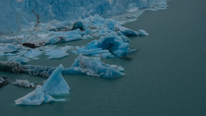 A melting glacier. A wall of blue ice in a glacial lake. Melted ice floes float in turquoise water....