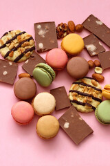 Pastel macarons, almond chocolate, peanut butter cookies and various nuts on bright pink background. Selective focus.