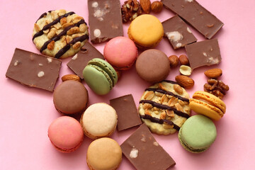 Pastel macarons, almond chocolate, peanut butter cookies and various nuts on bright pink background. Selective focus.