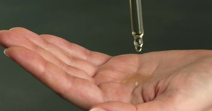 Drops of essential oil flow from the pipette onto the palm of the hand. 4K close-up video.