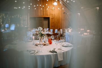 Valmiera, Latvia - August 25, 2023 - Wide shot of a wedding reception venue with set tables, floral centerpieces, and lit candles under wooden beams.