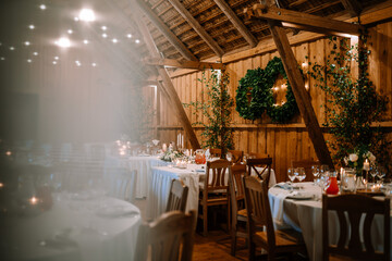 Valmiera, Latvia - August 25, 2023 - Rustic wedding venue with wooden beams, dining tables set with candles, and greenery on the walls.