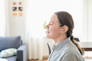 Portrait of young smiling woman with hearing aid on left ear at home