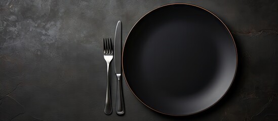 A moody copy space image capturing a close up view of a cutlery set consisting of an empty plate and a fork placed together on a black table This food concept photography evokes the essence of a sere