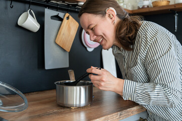 Portrait of young smiling woman with hearing aid on left ear cooking at home