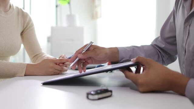 Woman signs a car purchase and insurance contract with a dealer, she pays money and receives the car keys.