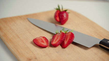 The strawberries are cut into slices. they lie on a wooden board and next to the knife