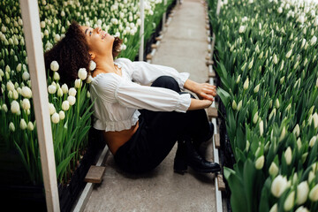 Female portrait of attractive darkskinned girl sitting on path among tulips in greenhouse