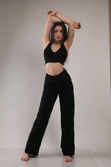 Portrait of a beautiful fashion model in the studio on a light background, wearing a black short clothes and trousers, barefoot