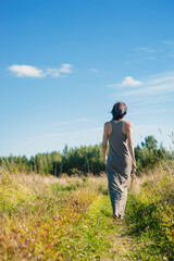 Fototapeta premium Back view of beautiful woman walking on the meadow in summer