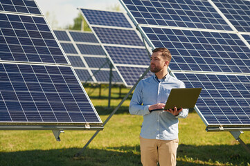 Holding laptop. Engineer with photovoltaic solar panels outdoors at daytime