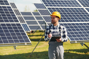 Using walkie talkie and holding notepad. Engineer with photovoltaic solar panels outdoors at daytime