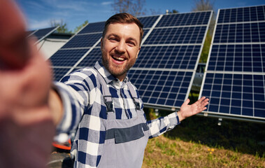Making a selfie, smiling. Engineer with photovoltaic solar panels outdoors at daytime