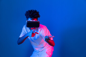 Young African American player using VR turn gun shooting hunter 3D gamer in hologram blue pink neon lighting wall connecting digital futuristic technology virtual reality metaverse world. Contrivance.