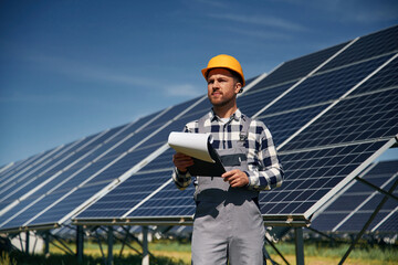 On the field with notepad in hands. Engineer with photovoltaic solar panels outdoors at daytime