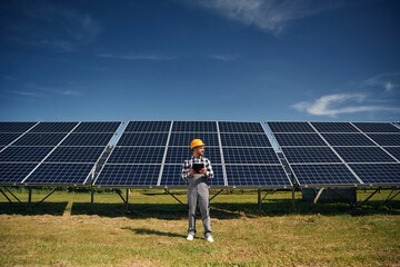 Black notepad in hands. Engineer with photovoltaic solar panels outdoors at daytime