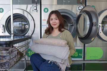 Beautiful woman enjoying clean clothes in the self service laundry with dryer machines on the background
