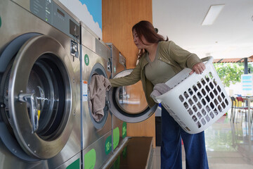 Beautiful woman enjoying clean clothes in the self service laundry with dryer machines on the...