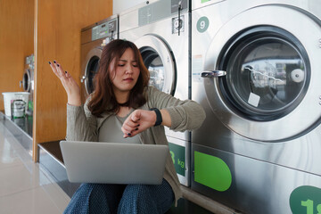 Beautiful woman working on laptop while waiting to do laundry