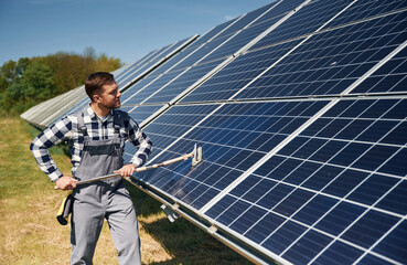 Mop in hands. Cleans the surface. Engineer with photovoltaic solar panels outdoors at daytime