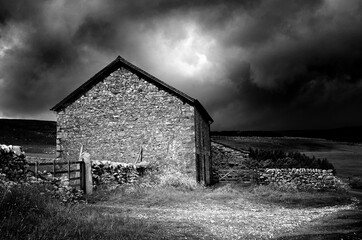 Black and white image of a old stone built farm house with stormy sky’s and dramatic lighting