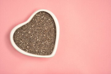 Photograph of chia seeds in heart shape white bowl with copy space on pink colour background. Top...