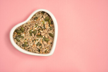 Photograph of seeds mix in heart shape white bowl with copy space on pink colour background....