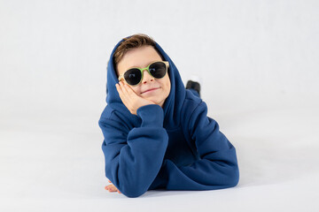 Cheerful boy in a blue tracksuit and sunglasses. Pretty boy,. Baby model. A little boy poses on a...