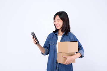 asian woman wearing denim jean holding parcel box while using mobile phone isolated on white studio background, Delivery courier and shipping service concept.