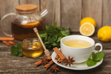 Fragrant hot tea with cinnamon stick and anise on a textured wooden background. A cup of hot tea with honey, lemon, mint and apples. Spicy tea with spices. Immunity tea. Health concept.Copy space.