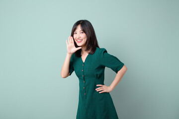 Happy Asian woman shouting above green dress poses against green background blank copy space for...