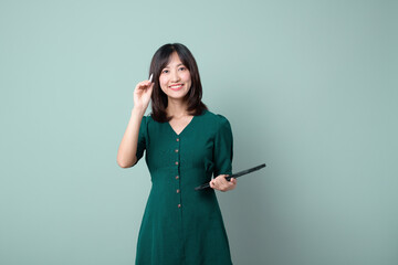 Happy asian woman smile and holding tablet isolated on light green background